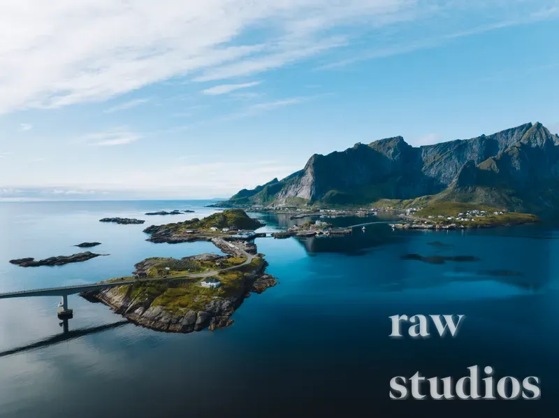 Et luftfoto av et kystlandskap med grønne øyer, bratte fjell og en vei som krysser vannet via en bro. Det blå havet og den klare himmelen skaper en lys og rolig stemning i dette maritime miljøet.